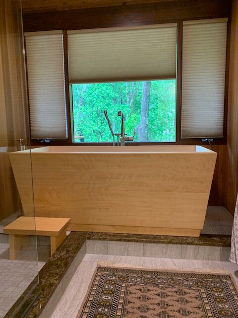 Custom size hinoki wood kyoto style ofuro soaking tub installed in a beautiful bathroom with wood paneling on the walls and two-tone tile floors. The pale golden hinoki wood features a silky rippled grain pattern.