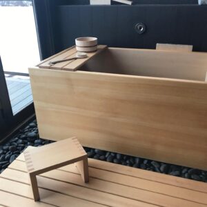 Hinoki Wood Onsen Ofuro Soaking Tub installed with hinoki wood bathing stool, tray, bath pail and sunoko. The tub is set on black river stone with black tile on the walls for a striking contrast with the blonde hinoki.