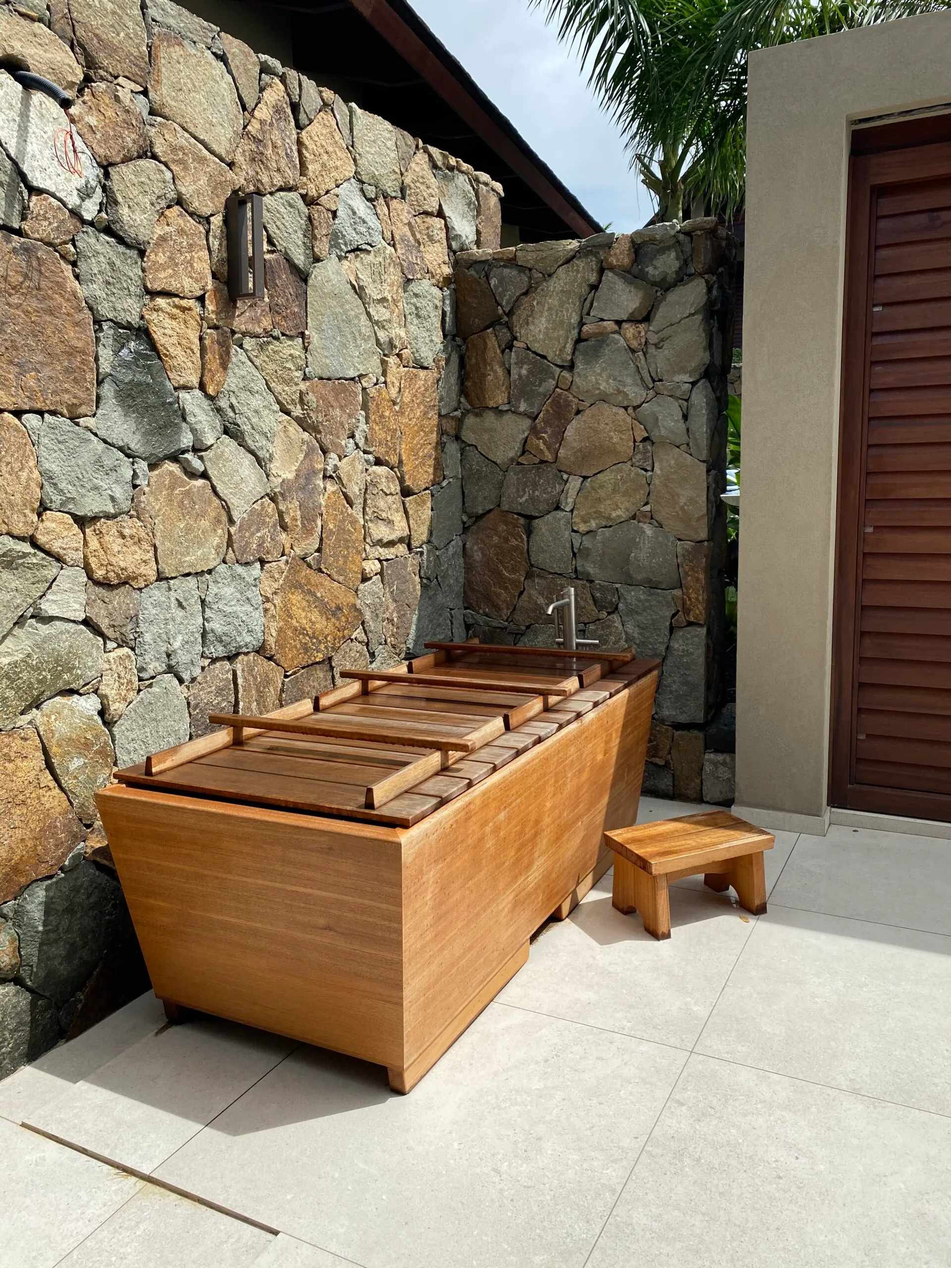 72 x 36 Zen Bathworks Teak Kyoto Ofuro soaking tub with cover and bathing stool outdoor installation by a stone wall